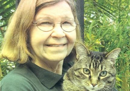 Picture of Kathy Wiberg outside with her cat in her arms; trees and greenery in the background. 